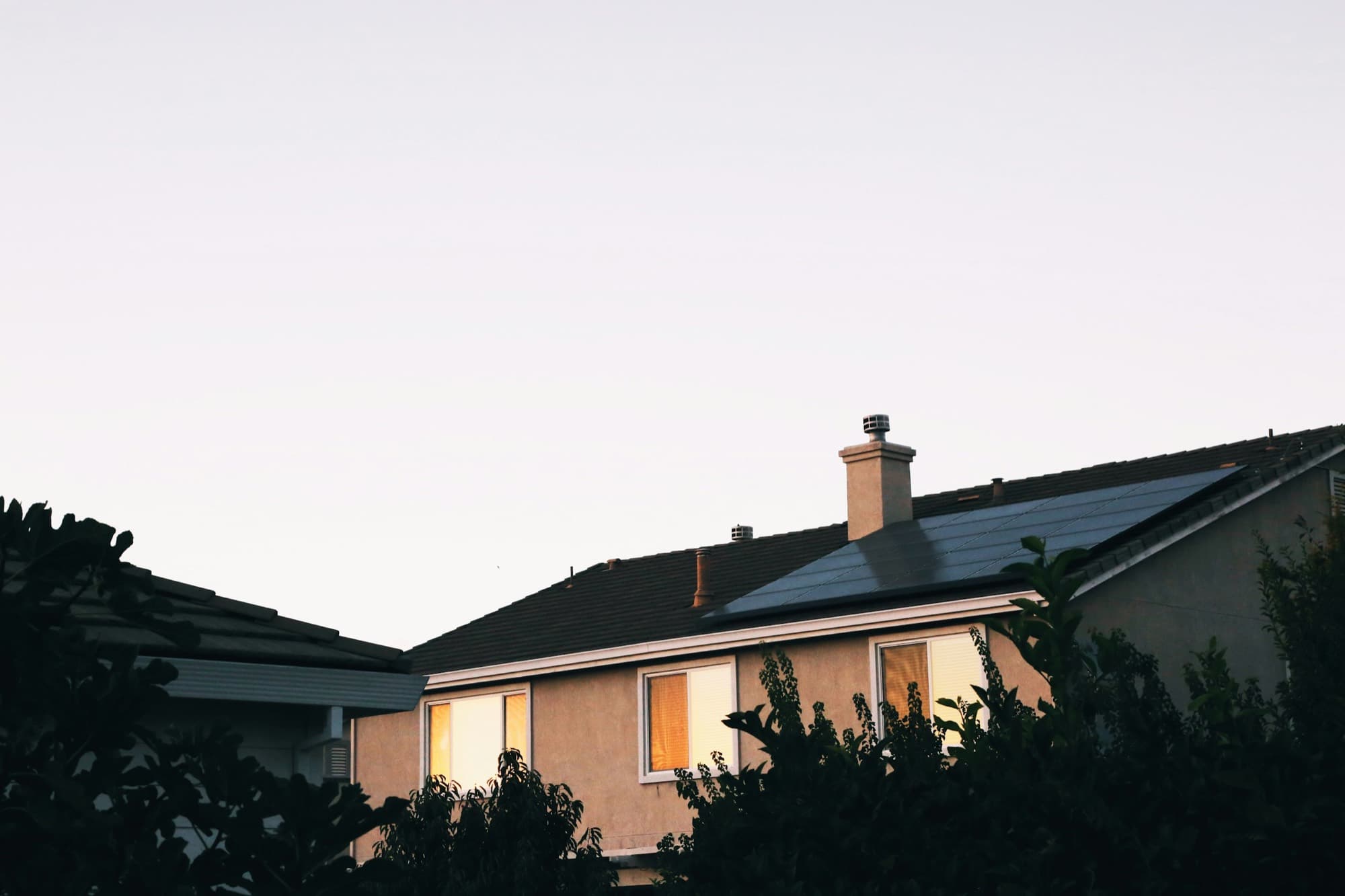 Home with rooftop solar at dusk, windows lit